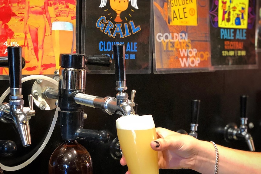 A hand holds a tall glass of pale beer under a tap.