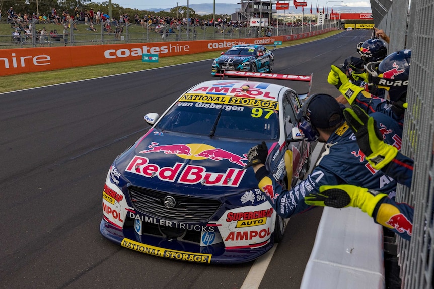 Race car cross the line with his team celebrating on the pit wall.