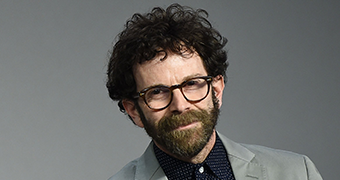 The screenwriter Charlie Kaufman in a grey suit in front of a grey background