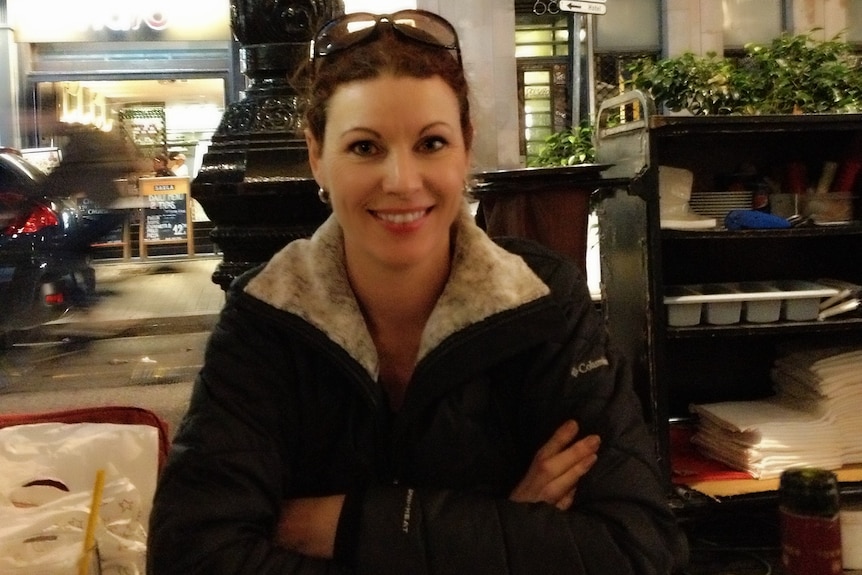 A young woman smiles while posing for a photo at an outdoor table at a restaurant at night.