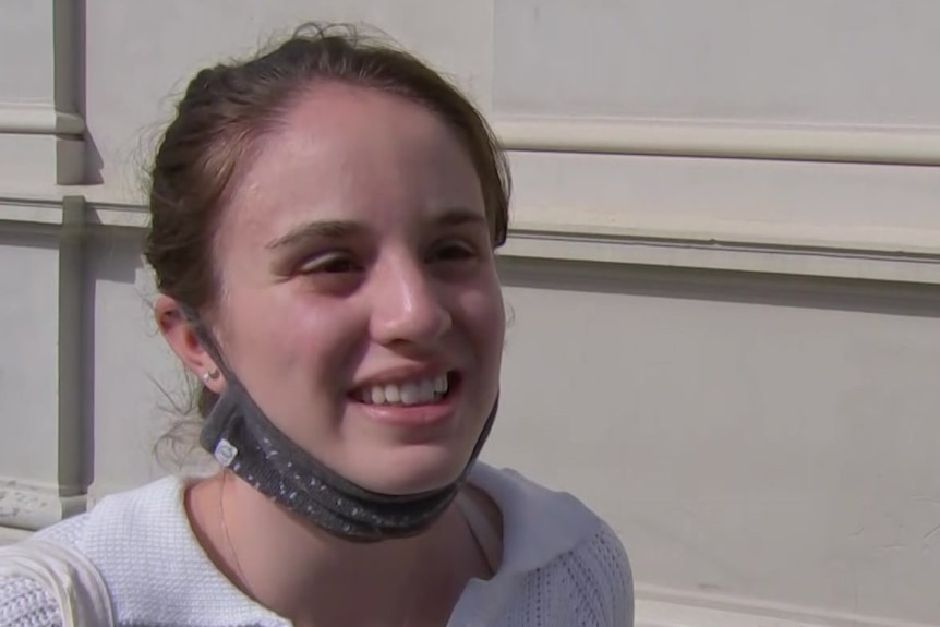 A woman standing outside with a mask pulled down under her chin.