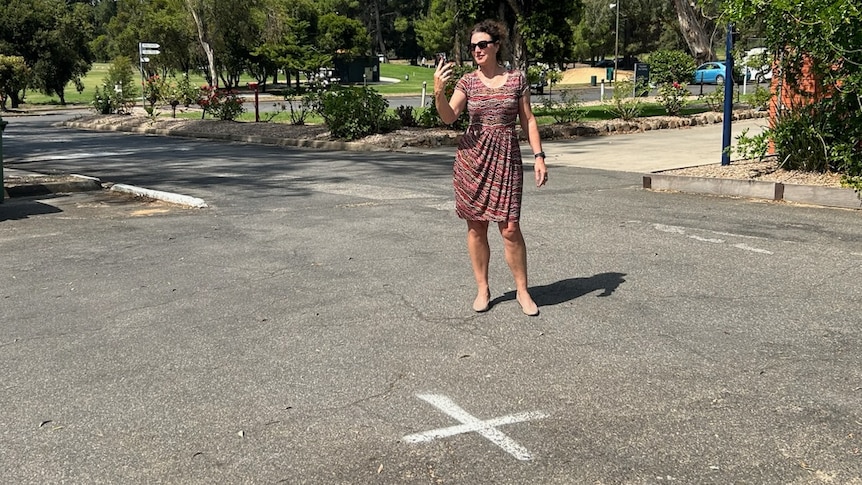 A woman making a phone call in a parking lot with an X marking the spot