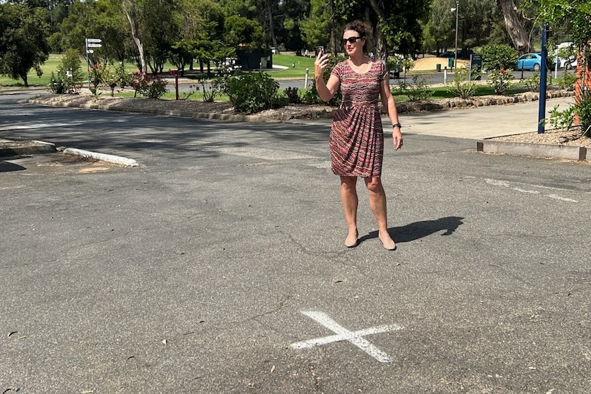 A woman making a phone call in a parking lot with an X marking the spot