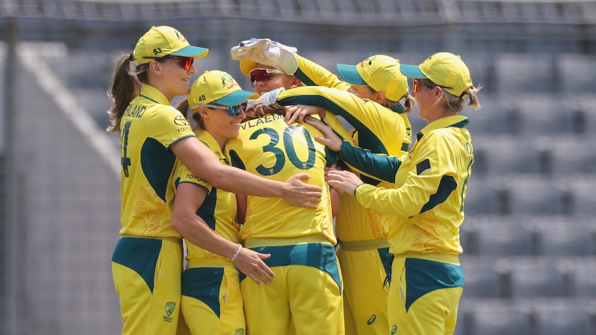A group of Australian women's cricketers gather together on the pitch to celebrate.