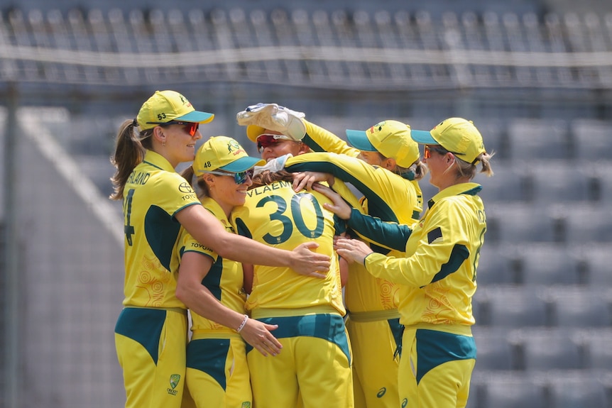 A group of Australian women's cricketers gather together on the pitch to celebrate.