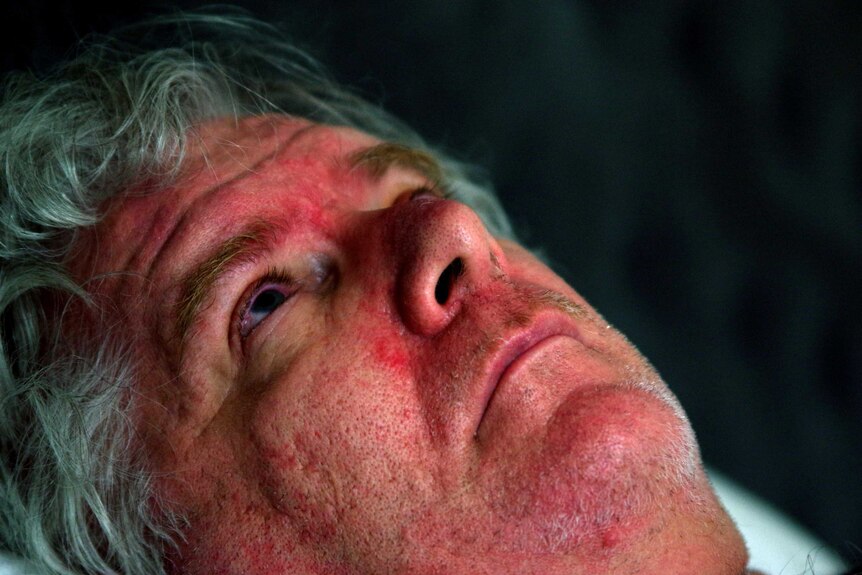 A close-up shot of the face of a man with grey hair lying down looking up.
