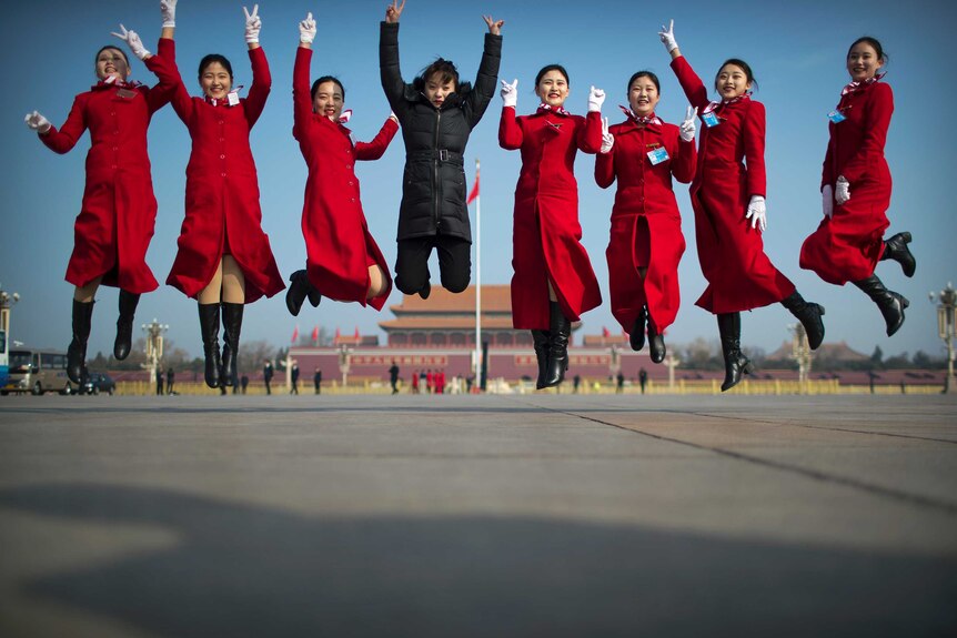 Bus ushers leap as they pose for a group photo in front of the Forbidden City.