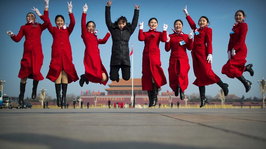 Bus ushers leap as they pose for a group photo in front of the Forbidden City.