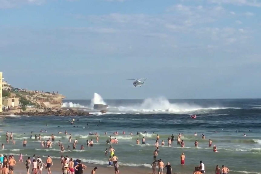 helicopter hovering over rocks at a beach