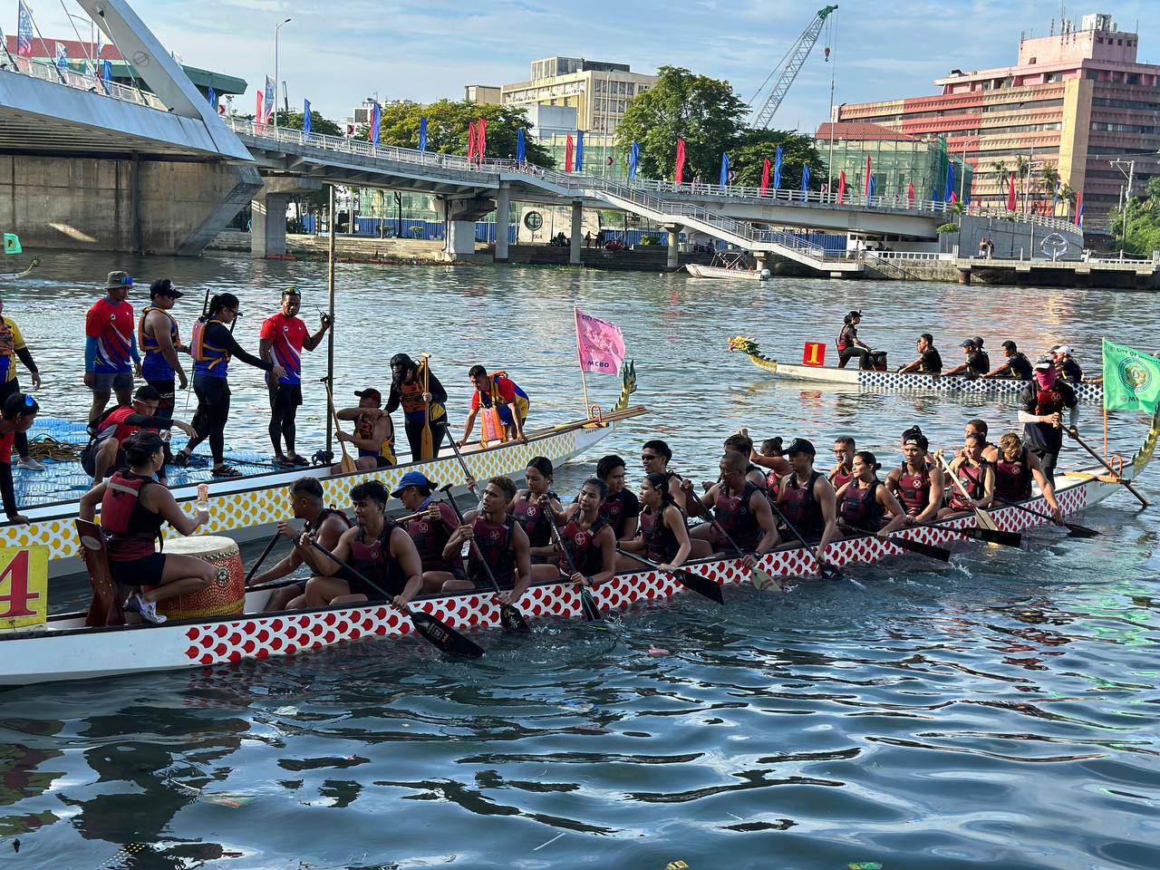 Três barcos-dragão cheios de remadores se preparando para correr no rio.