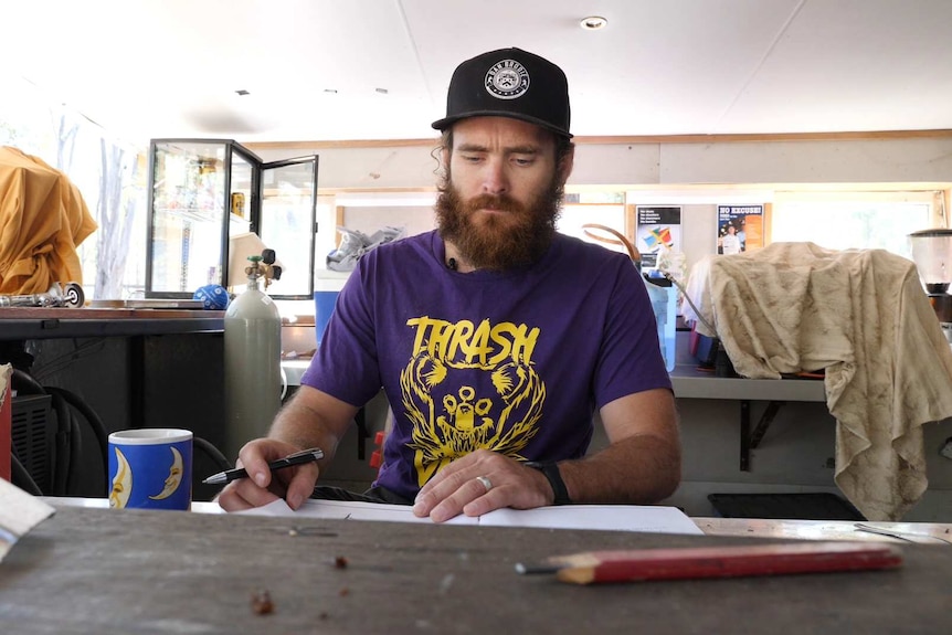 A man with a beard in a purple rock and roll shirt looks over some paper work