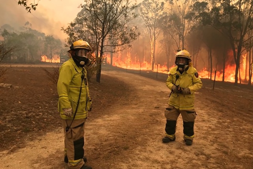 Two firefighters wearing retardant jackets and breathing apparatus near a large bushfire
