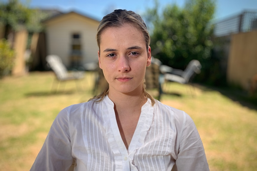 A young woman is pictured in a backyard, looking into the camera with a serious expression on her face.
