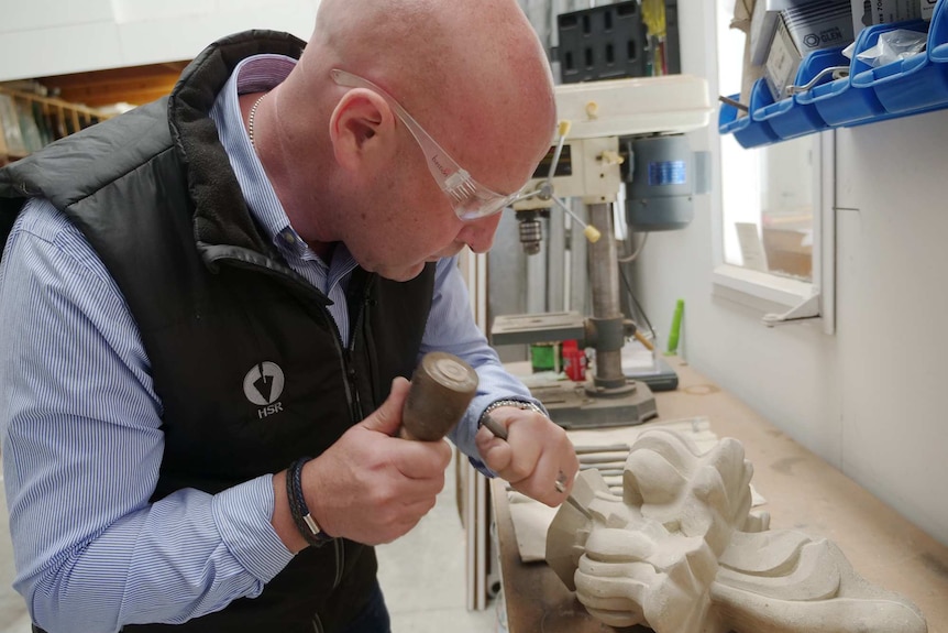 Martyn Lambourne uses a chisel to work on a large piece of decorative sandstone