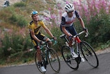 Australia's Richie Porte wearing white rides up a French peak, mouth open as another cyclist smiles from behind.