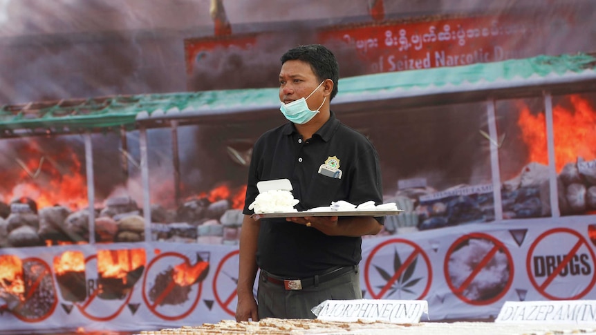 A police officer holds seized drugs in front of a big fire