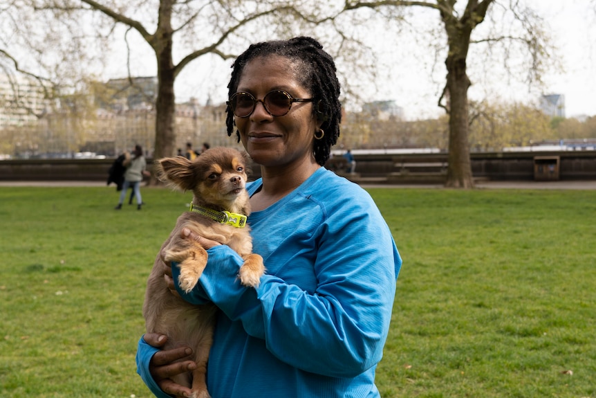 A woman wearing sunglasses holds a dog in a park.