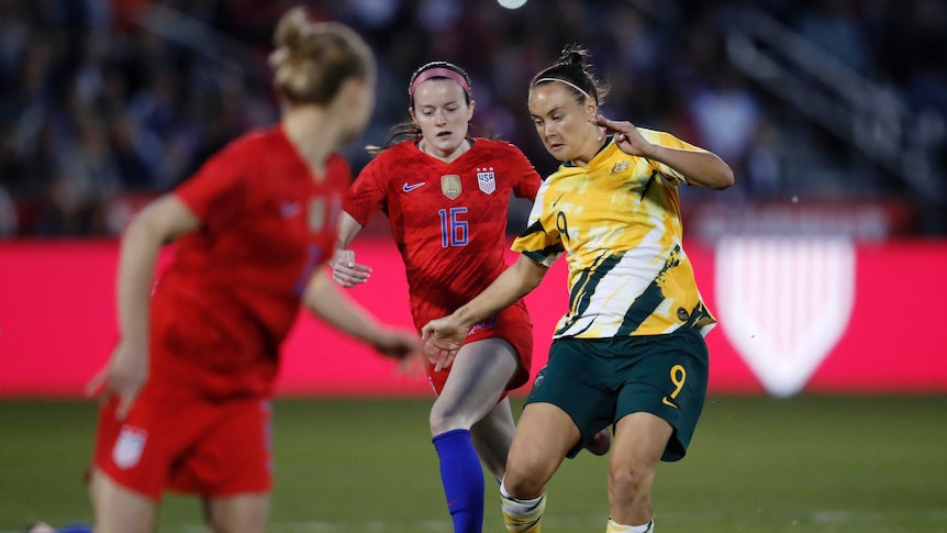 Caitlin Foord in yellow passes the ball forward with two, red shirted players chasing