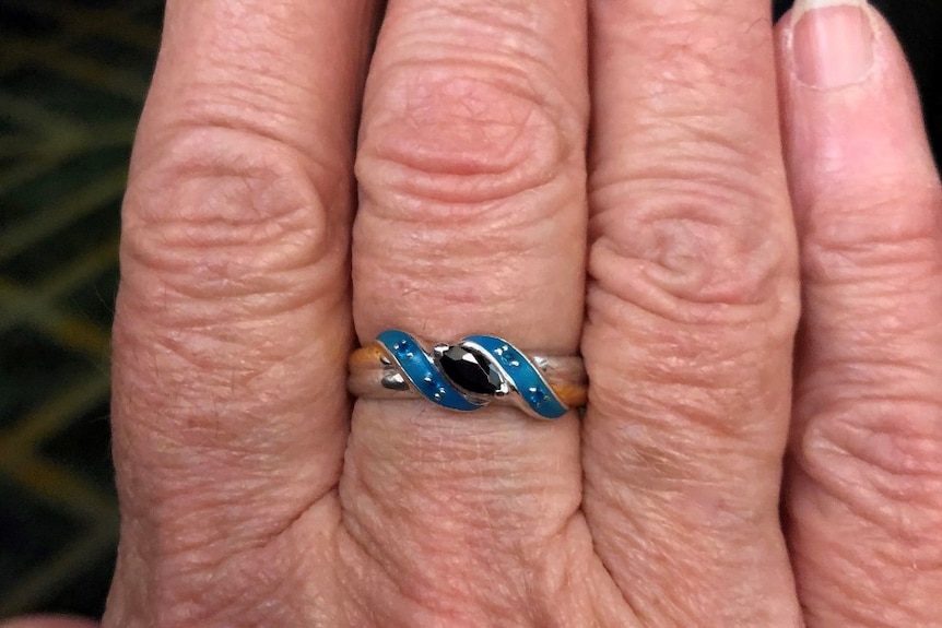 A woman's hand wearing a ring with a black stone blue surround and white and yellow gold band with "Go the Panther's" inscribed.