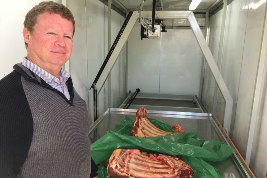 A man stands next to a tray of meat in an industrial building.