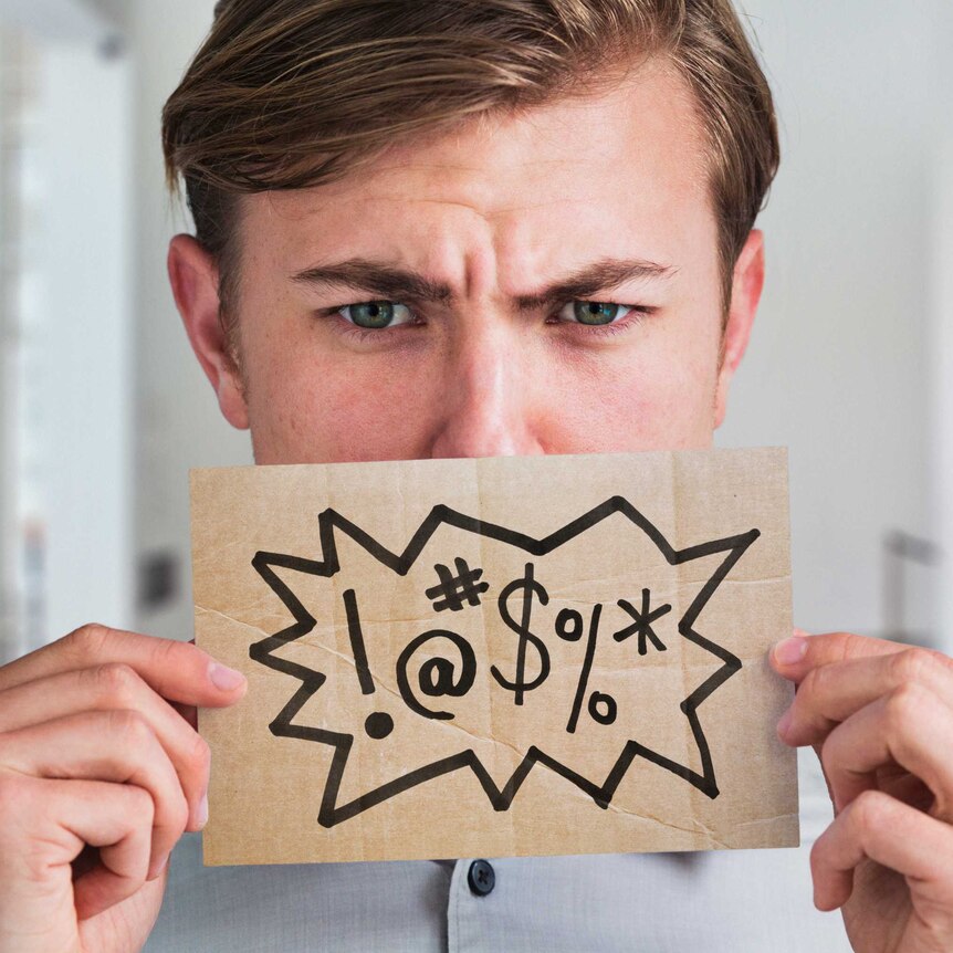 Head shot of man with frown on his face. He is holding a piece of cardboard to his lips with symbols drawn to indicate swearing.