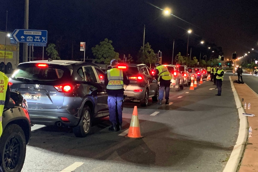 A long row of cars, each with a police officer nearby, at a border checkpoint.