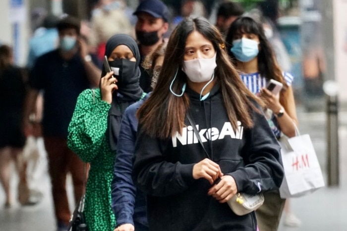 Three mask-wearing women walk down a city street.