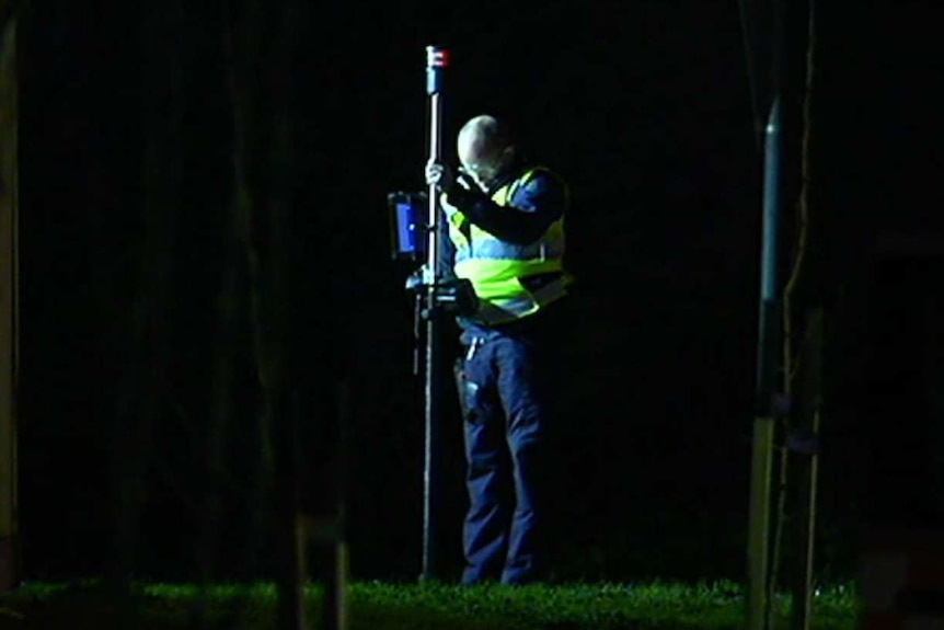 A police officer takes a measurement at the scene of a car crash.