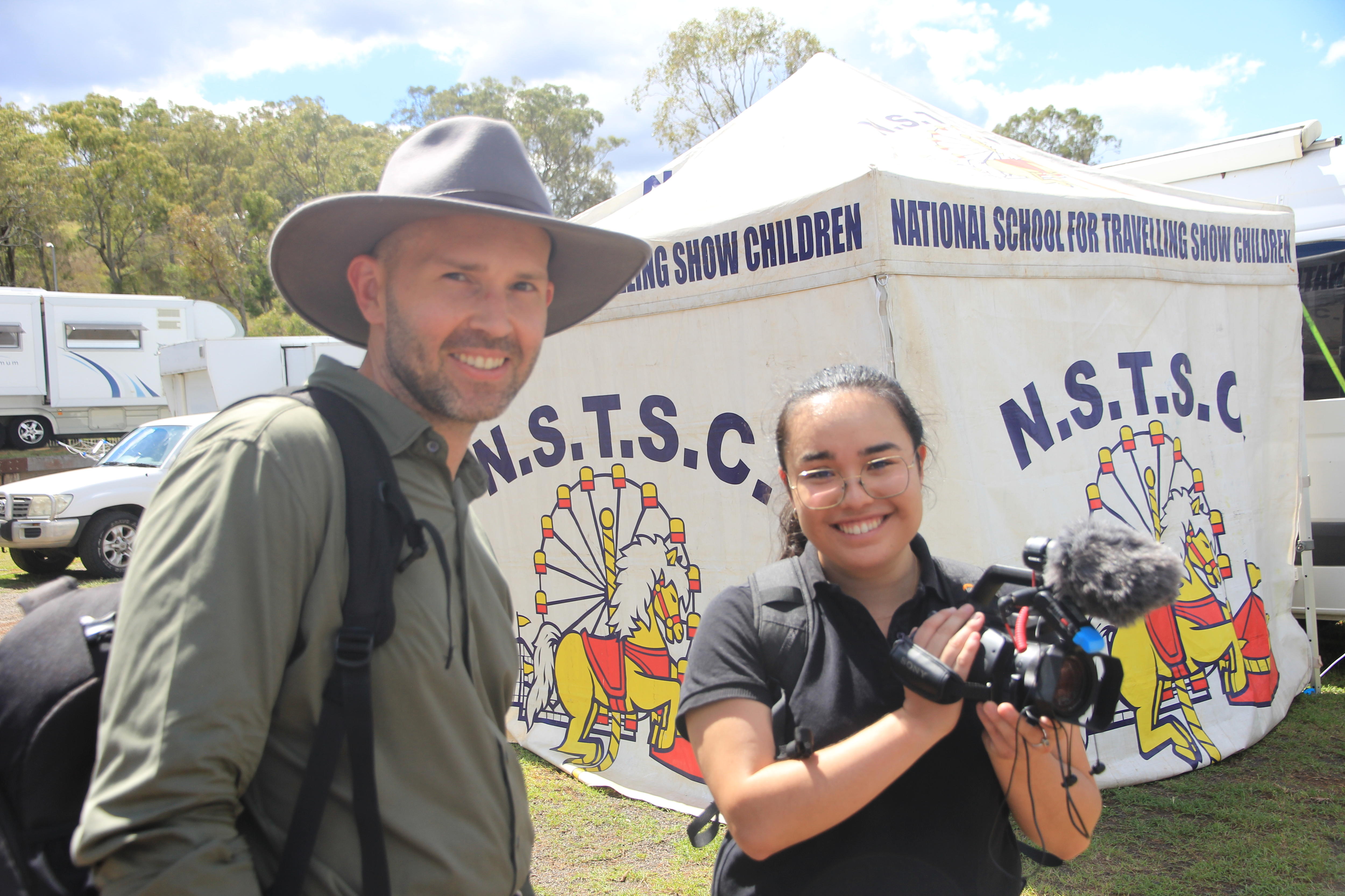man in broad hat and woman with glasses and camera smiling, tent behind them
