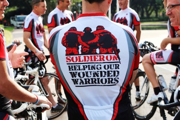 Cyclists wearing Soldier On shirts stand in a group with their bikes.