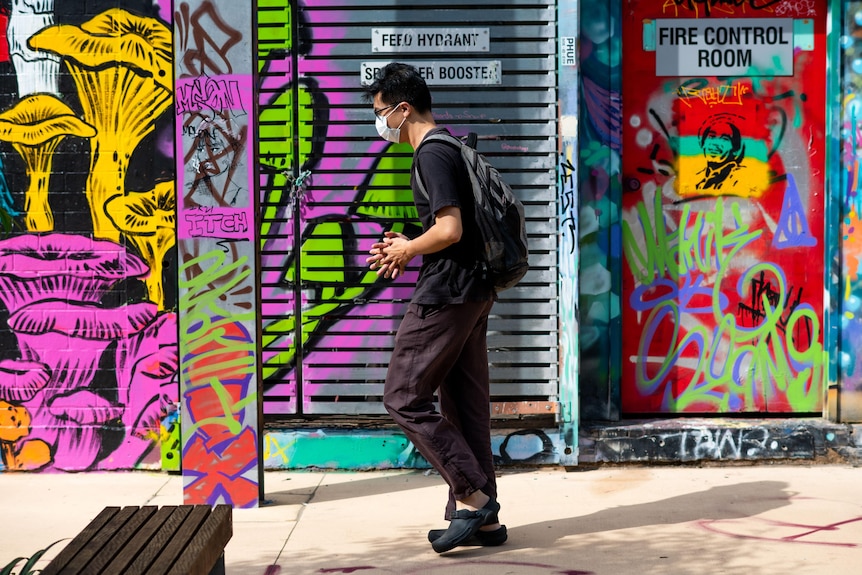 A man wearing a mask walking past a wall of colourful graffiti
