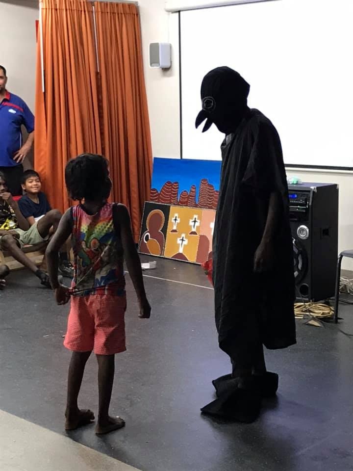 A small child looks at a man dressed in a black bird costume