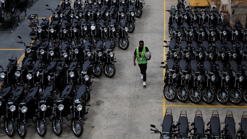 A man in a high-vis vest walks between rows of neeatly parked motorcycles