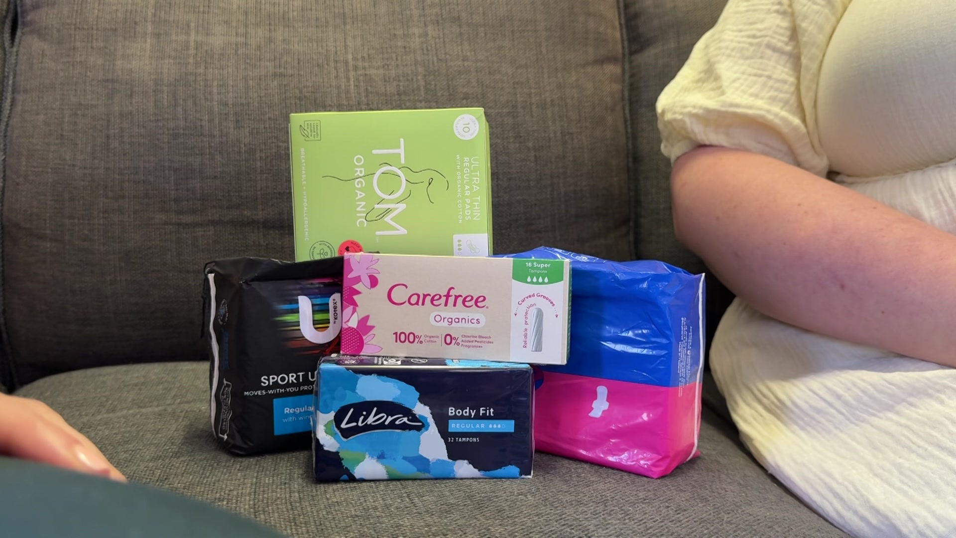 Imagem de produtos vintage em um sofá ao lado de uma mulher de vestido amarelo que está apenas parcialmente visível.