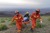 Rescue workers carry a stretcher with mountain view behind of vast Yellow River landscape. 