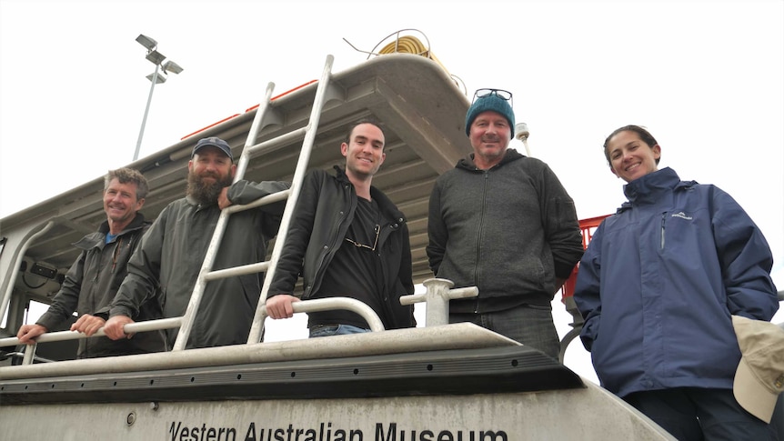 Four men and one woman stand on board a boat.