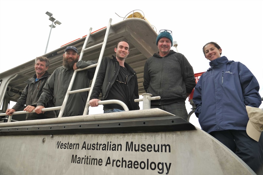 Four men and one woman stand on board a boat.