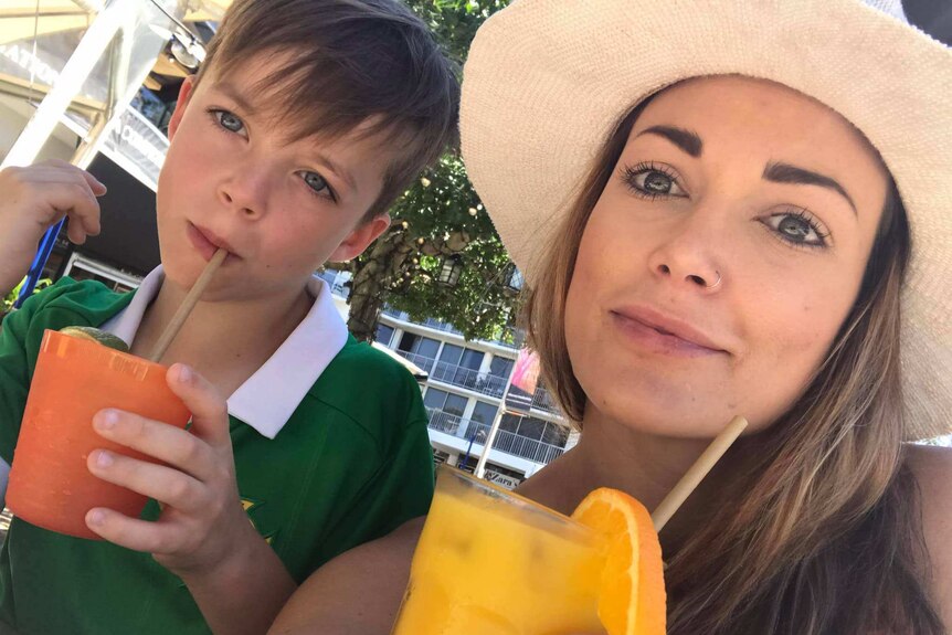 Caucasian woman and young son hold tropical drinks looking to the camera