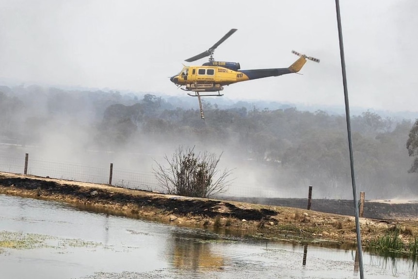 a yellow helicopter drops water on a burnt land