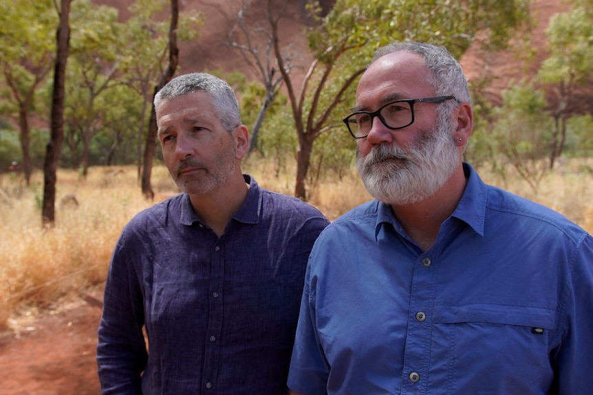 Two men wearing blue shirts standing in the outback.