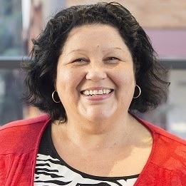 Portrait photo of Bronwyn Carlson, wearing black and white top and red jacket.