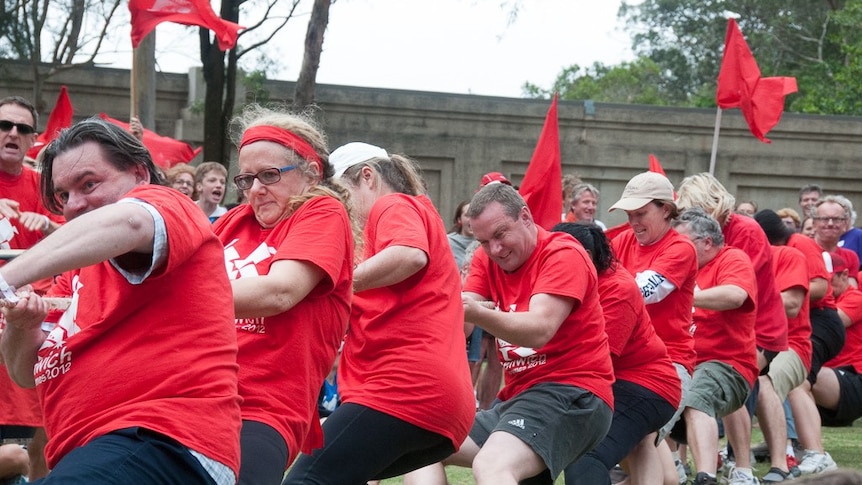 A lind of people wearing red t-shirts pull on a rope in a game of tug-of-war