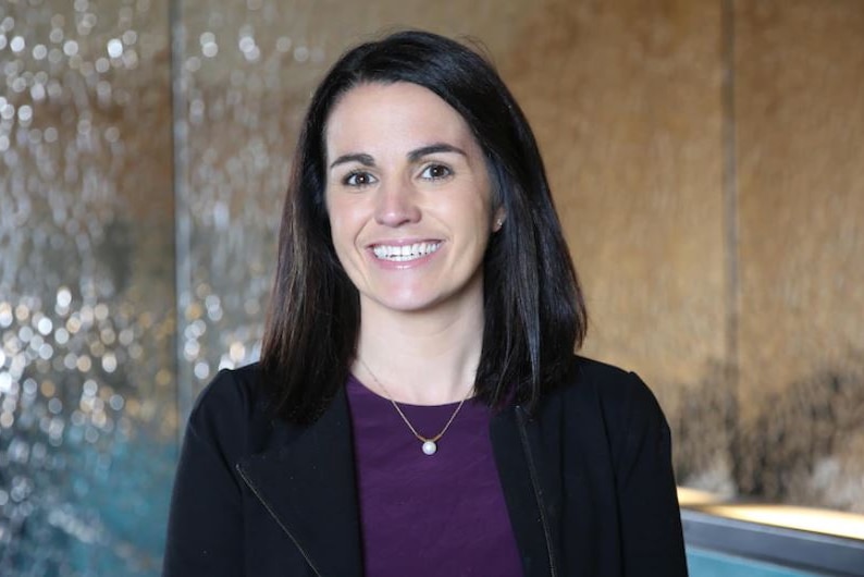 A dark-haired woman smiles at the camera in a office.