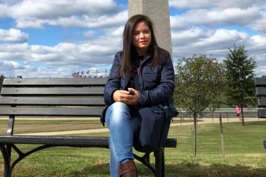 A woman with long dark hair sitting in puffy jacket on park bench