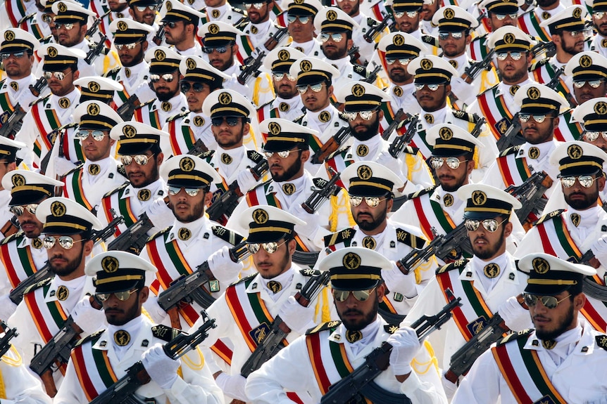 Rows and rows of members of Iran's Revolutionary Guard march holding guns and wearing aviator sunglasses in white uniforms.