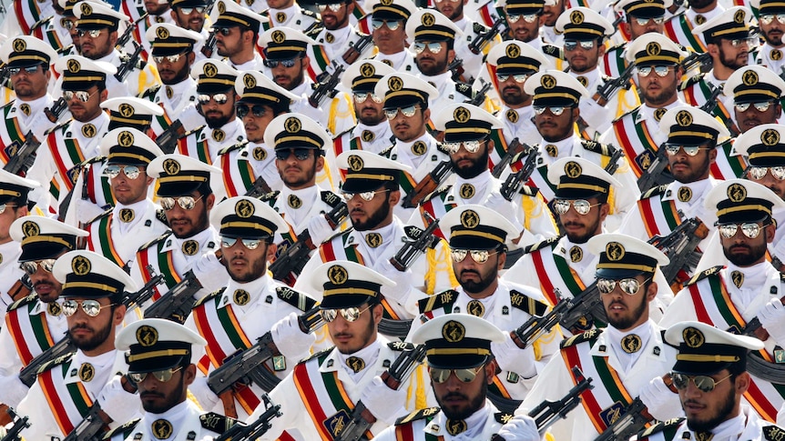 Rows and rows of members of Iran's Revolutionary Guard march holding guns and wearing aviator sunglasses in white uniforms.