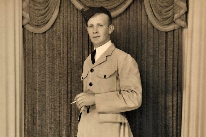 Sepia photo of man in suit and beret0style had with cigarette in hand, photographed standing against heavy drapes.