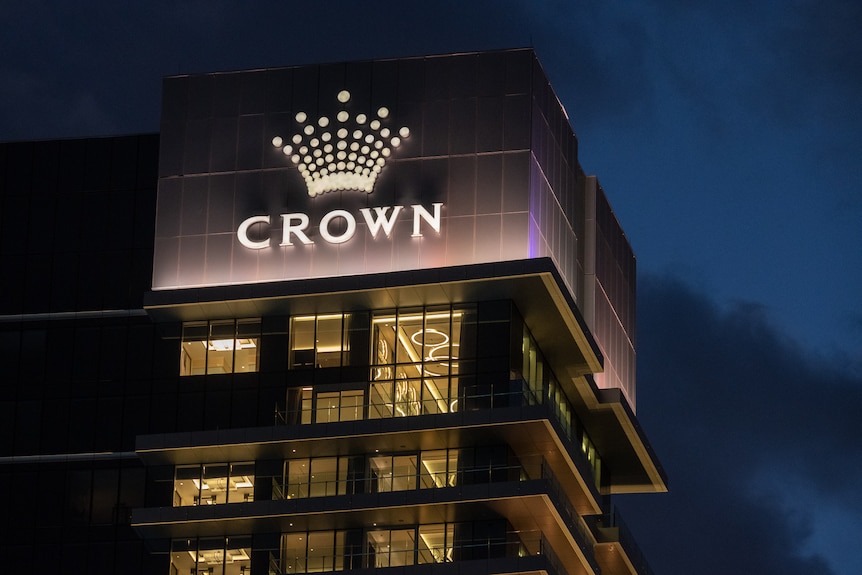 Tall buildings in the dark with lights on with an illuminated sign with the word Crown below a crown symbol.