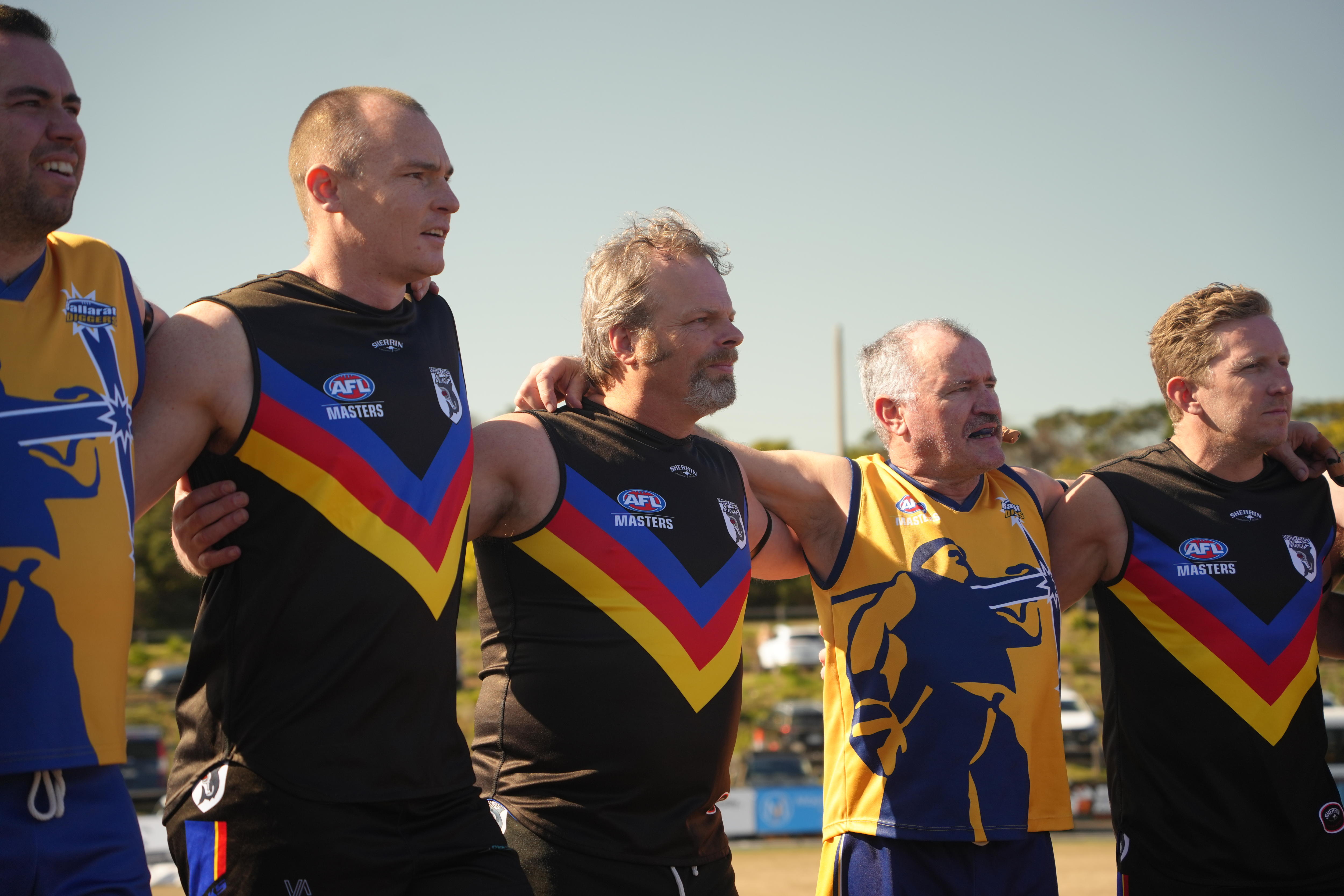 Five players from the Diggers and Sharks stand fully uniformed, arm-in-arm in the sun, before the game