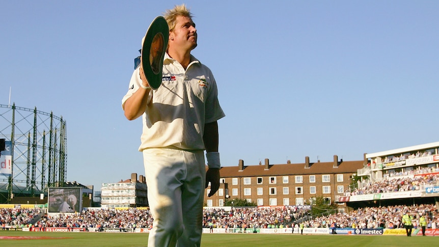 A man holds a wide brimmed hat in his hand and acknowledges the crowd